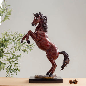 Red bronze rearing stallion sculpture front view displayed with greenery and framed art