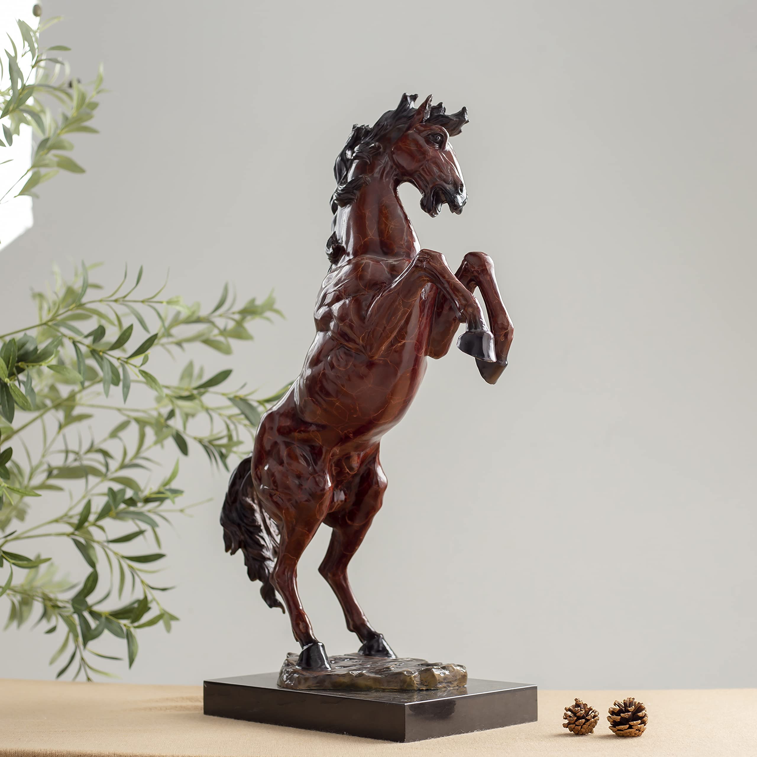 Red bronze rearing stallion sculpture side view displayed with greenery in indoor setting