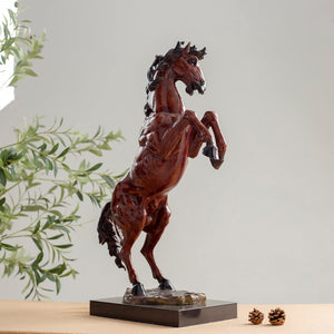 Red bronze rearing stallion sculpture side view displayed with greenery in indoor setting