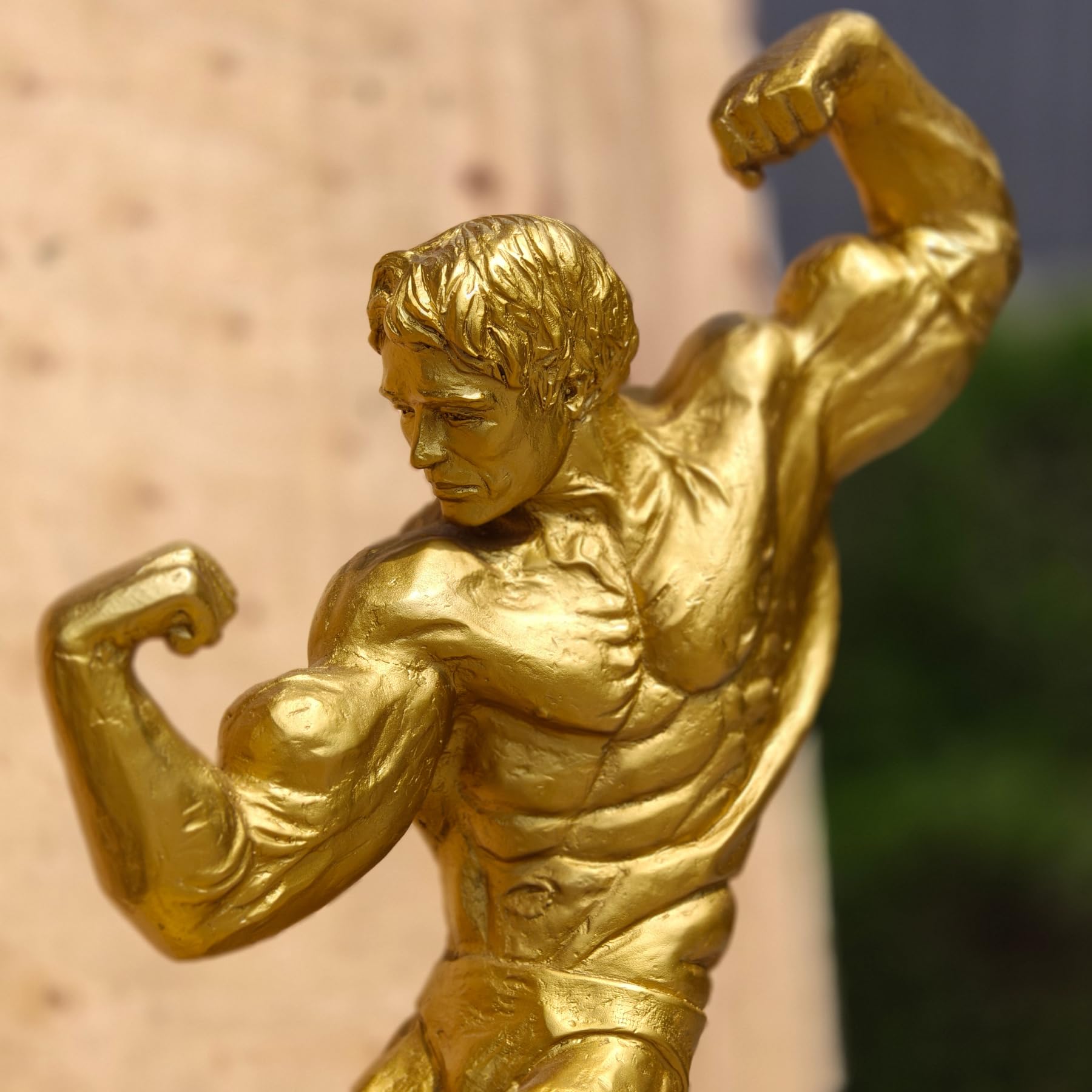 Close-up side view of gold finish bodybuilder bronze sculpture showing detailed muscle anatomy