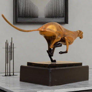 Close-up detail of gold running cheetah sculpture on black marble base in indoor decor