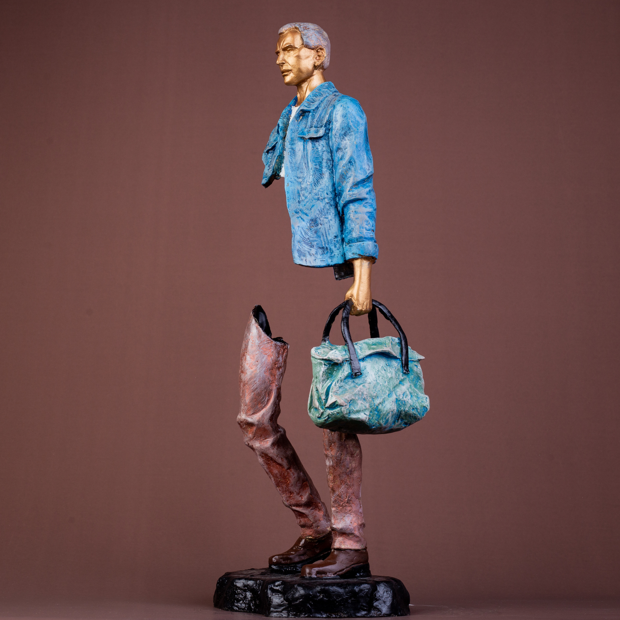 Hand-painted bronze sculpture of a man in a blue denim jacket holding a bag