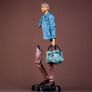 Hand-painted bronze sculpture of a man in a blue denim jacket holding a bag