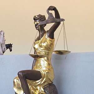 Close-up detail of large gold bronze Lady Justice Themis statue showing gilded finish and scale texture