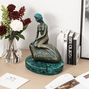 Little mermaid bronze sculpture displayed on bookshelf beside roses books