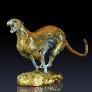 Modern abstract bronze and gold cheetah sculpture on rock base displayed against dark background