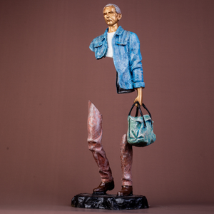 Modern bronze traveler statue with blue jacket and bag, partial body design on pedestal