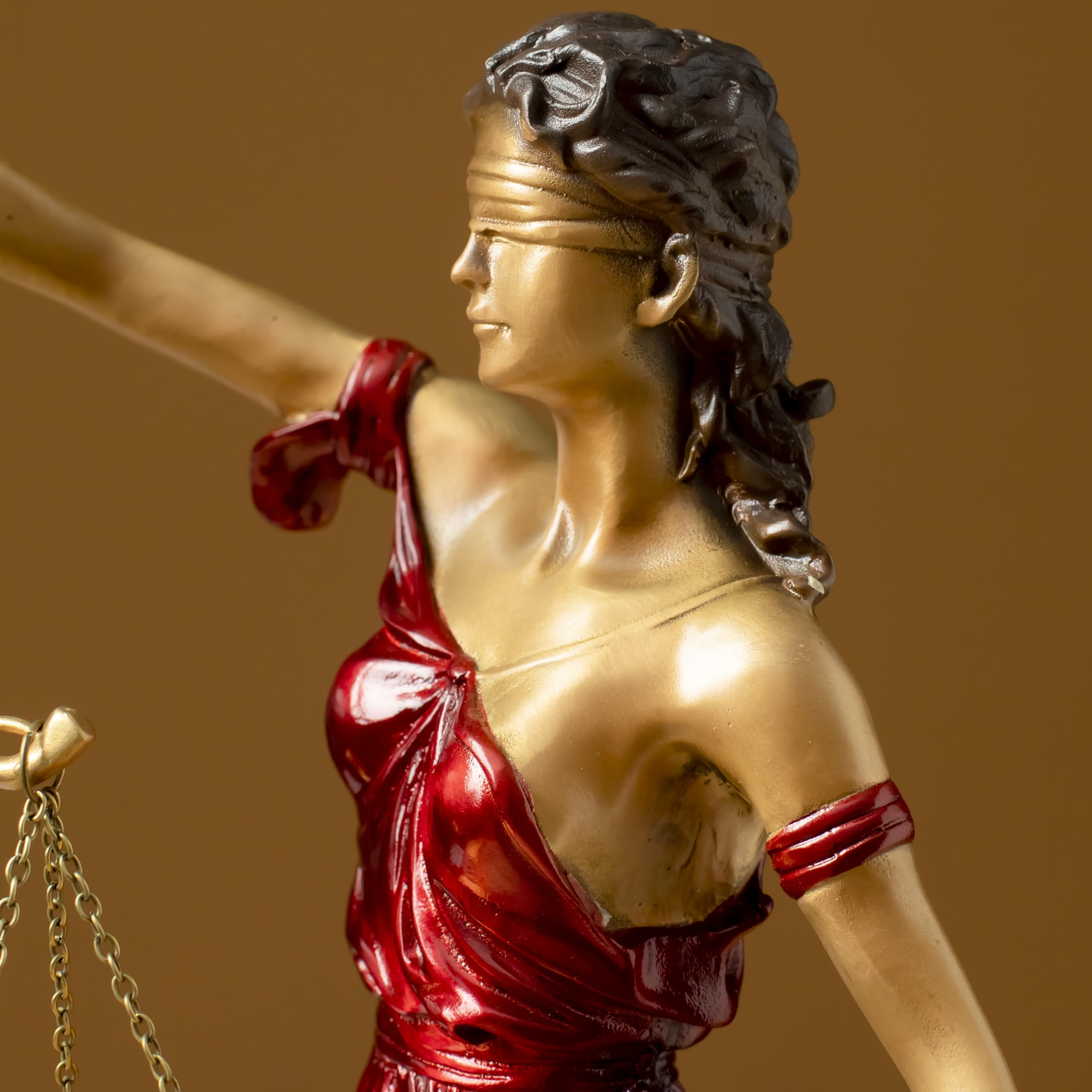 Close-up front view of red Lady Justice Themis statue on brown background showing scale and robe detail