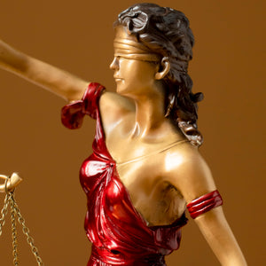 Close-up front view of red Lady Justice Themis statue on brown background showing scale and robe detail