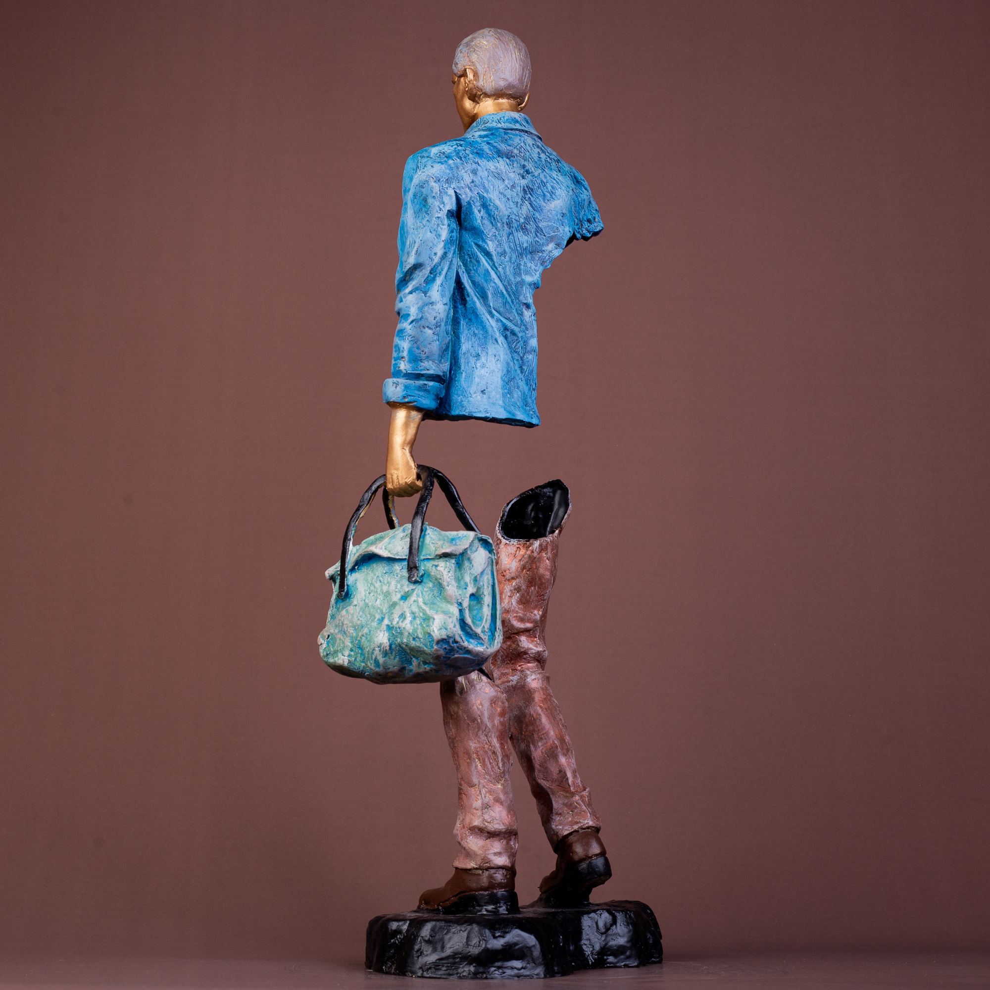 Bronze sculpture of a man holding a sage green handbag, wearing a blue jacket and brown pants