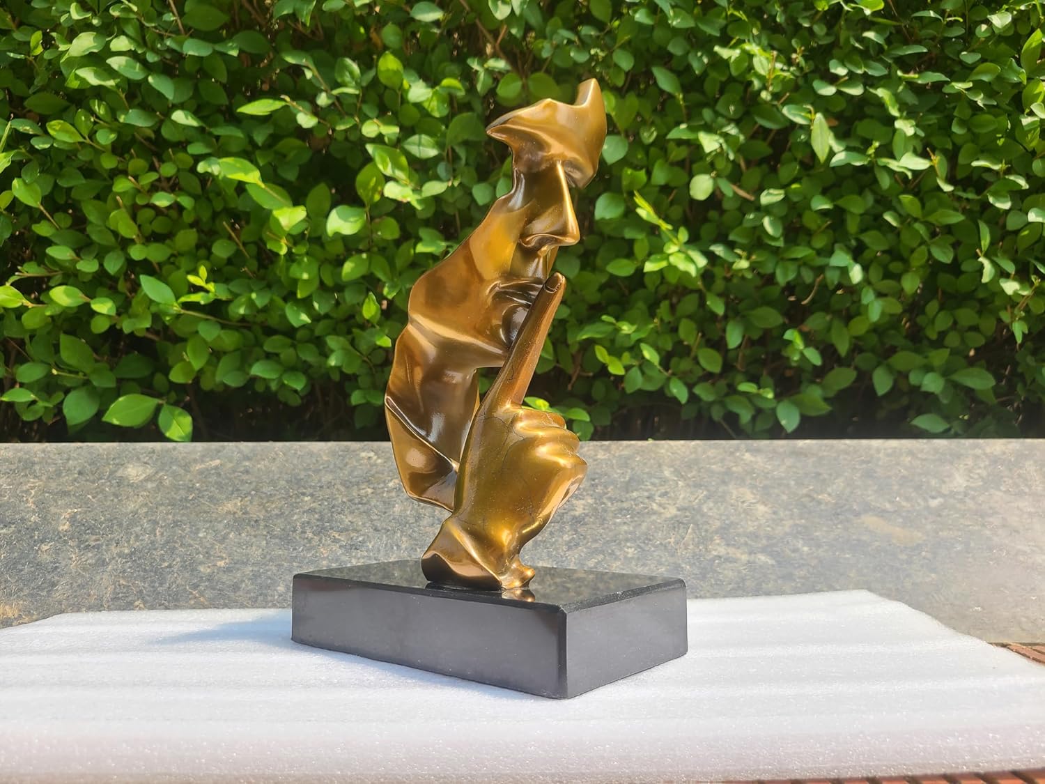 Left angle view of gold Silence is Gold thinker bronze figurine on outdoor marble base