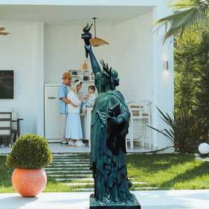 Verdigris blue bronze Statue of Liberty displayed near indoor staircase with potted plant decor