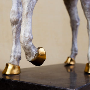 Close-up detail of white bronze horse sculpture showing golden hooves on black marble base