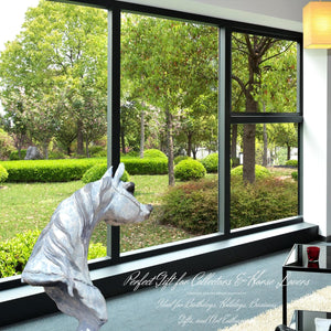 White patina bronze Arabian horse head sculpture displayed by floor-to-ceiling window with garden view